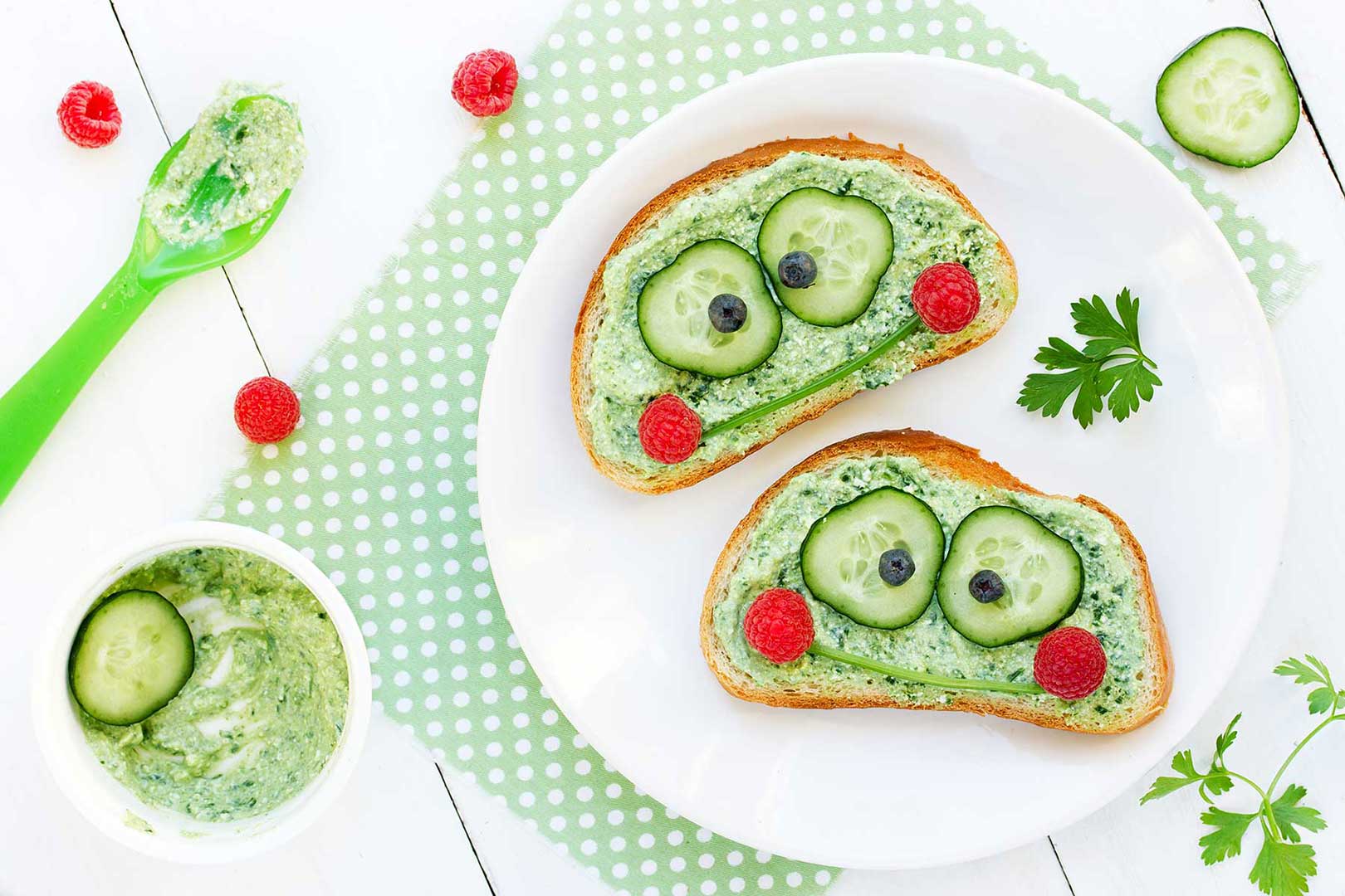 Grüner Brotaufstrich mit Gurke und Obst als lustiges Gesicht